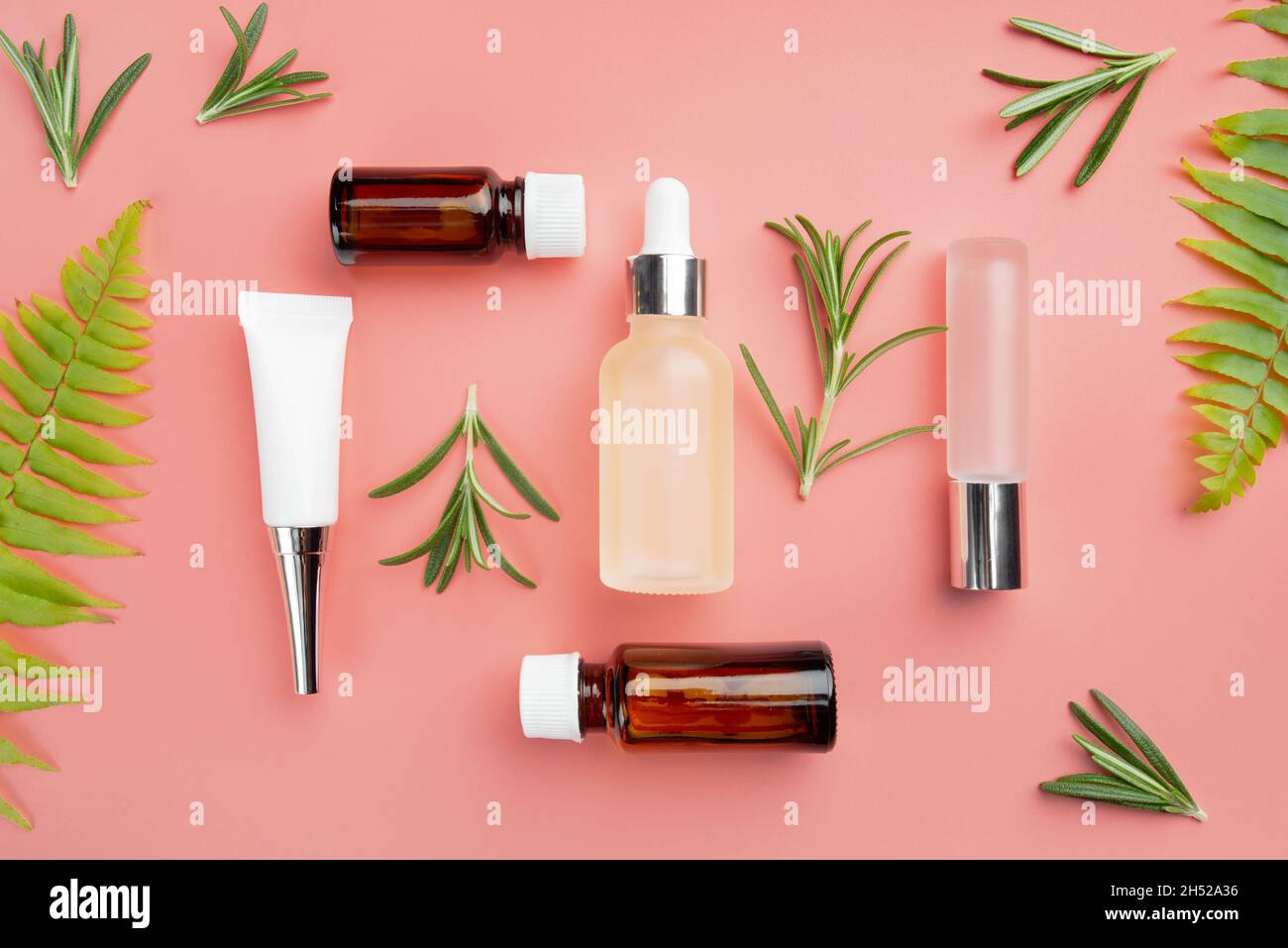 Bouteilles cosmétiques en verre et en plastique sur fond rose avec des feuilles de fougère et de romarin Banque D'Images