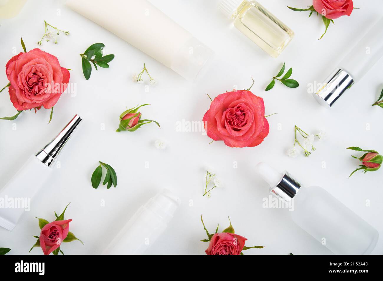 Déposez les bouteilles et les contenants de cosmétiques avec des roses roses et des feuilles vertes sur la table blanche Banque D'Images