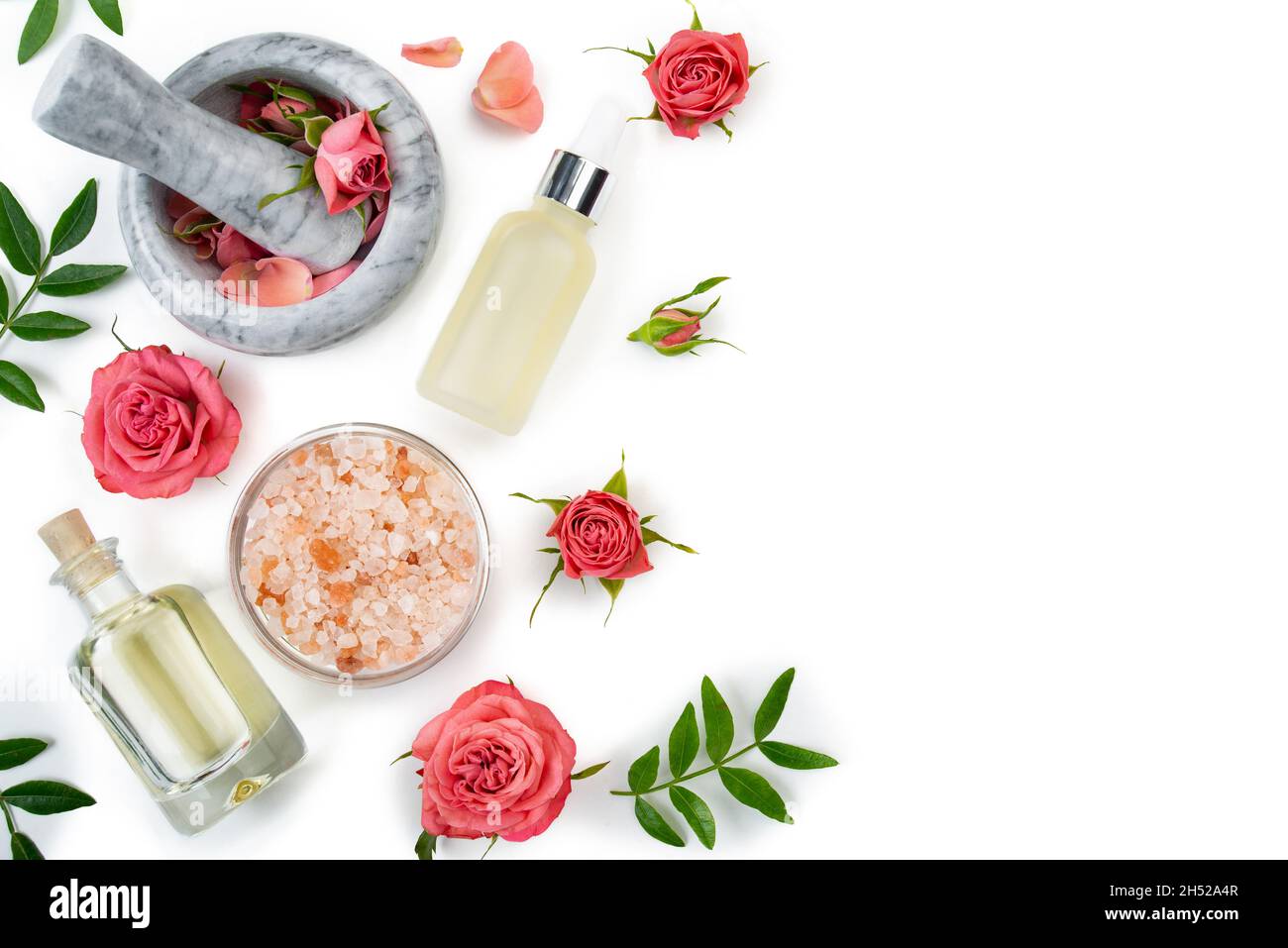 Conception plate de la rose cosmétique concept de mortier et pilon avec boutons roses avec le sel compte-gouttes et la bouteille d'huile sur fond blanc Banque D'Images
