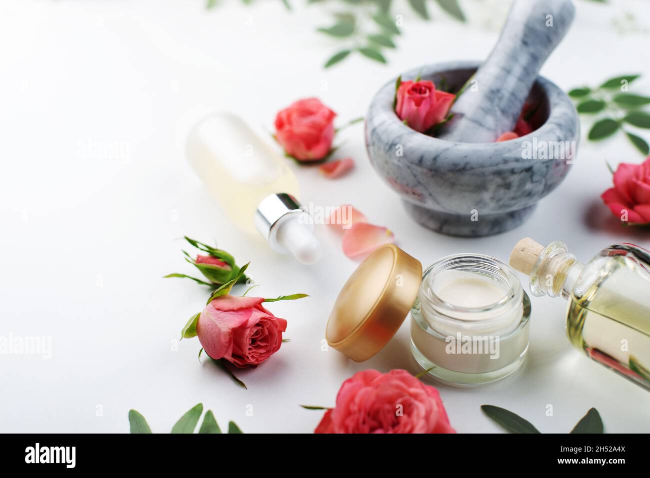 Fait main rose cosmétiques concept de mortier et pilon avec boutons roses avec compte-gouttes et bouteilles avec sérum et huile sur fond blanc Banque D'Images
