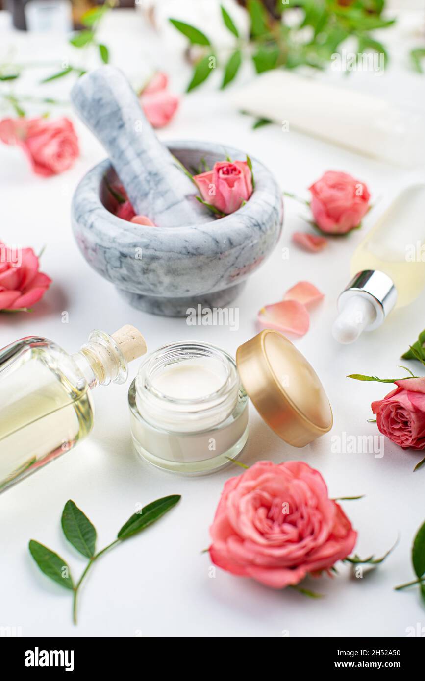 Fait main rose cosmétiques concept de mortier et pilon avec boutons roses avec compte-gouttes et bouteilles avec sérum et huile sur fond blanc Banque D'Images