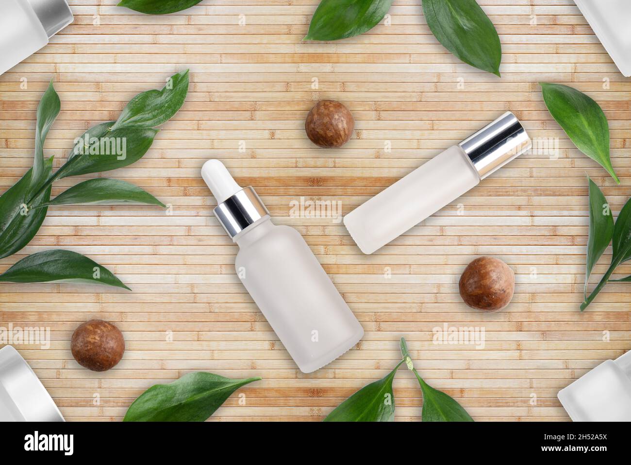 Fond plat et inclinable des bouteilles avec des cosmétiques pour noix de macadamia et des feuilles sur un tapis de bambou.Concept de cosmétiques naturels Banque D'Images
