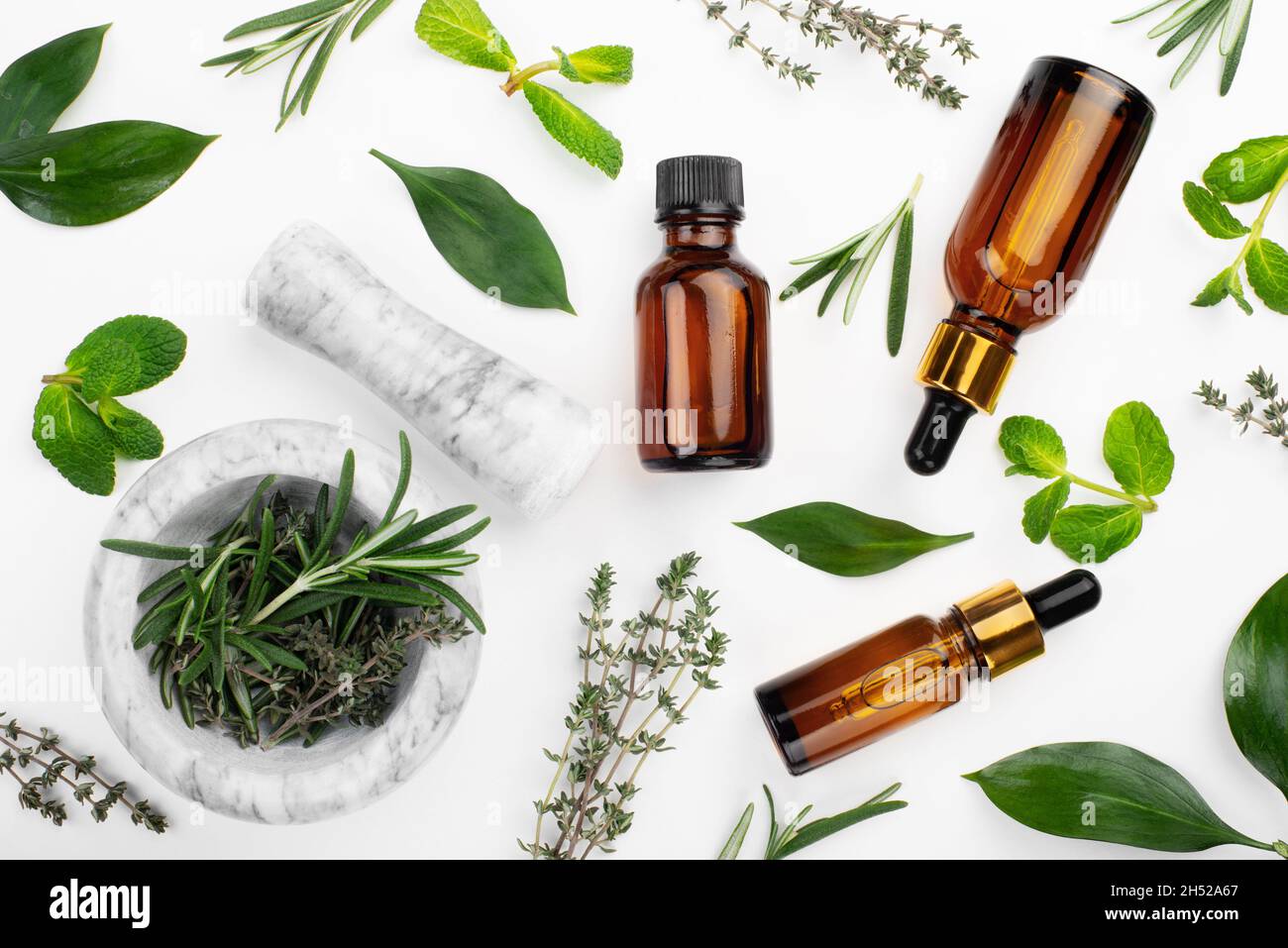 Flacons compte-gouttes avec huile et mortier avec herbes sur table blanche.Concept de cosmétiques à base de plantes Banque D'Images