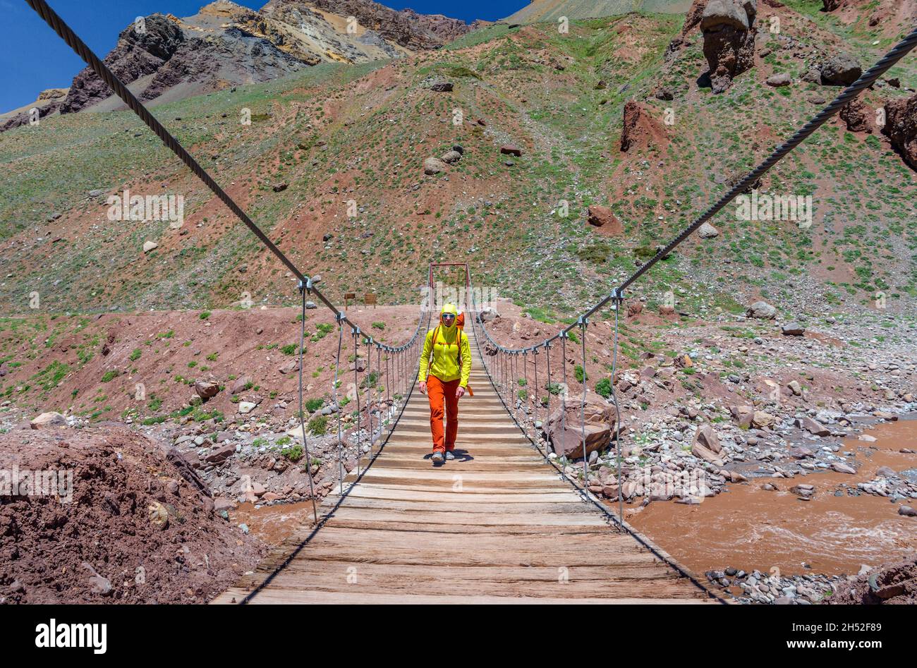 Homme avec un sac à dos traversant la rivière sur un pont suspendu au parc provincial d'Aconcagua en randonnée jusqu'au camp de base de la Plaza de Mulas Banque D'Images