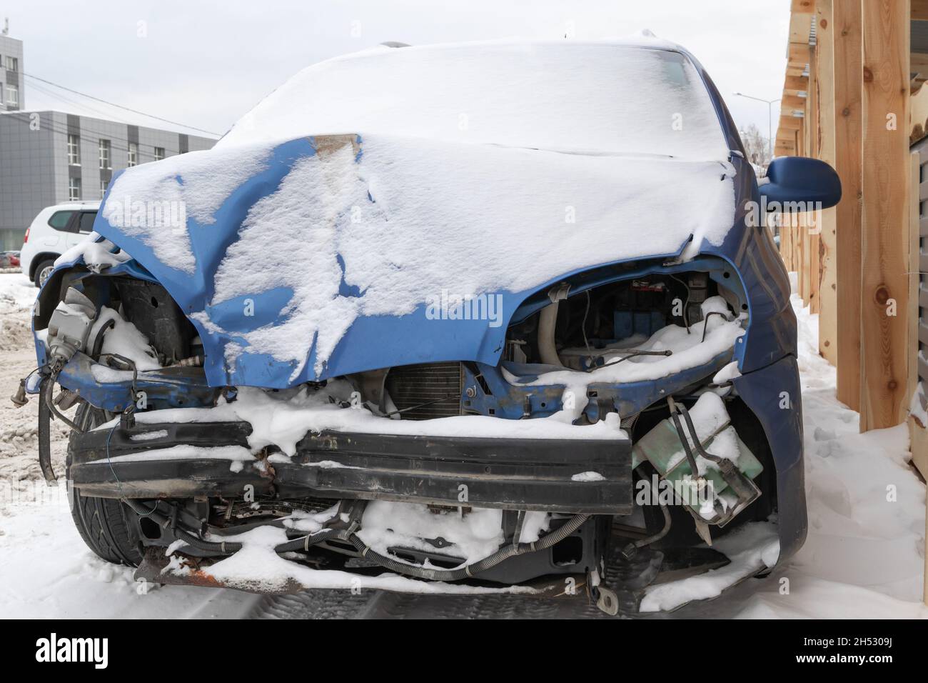 la voiture bleue s'est écrasée sans phares ni pare-chocs après un accident garé par la route sous une couche de neige une journée d'hiver froide Banque D'Images