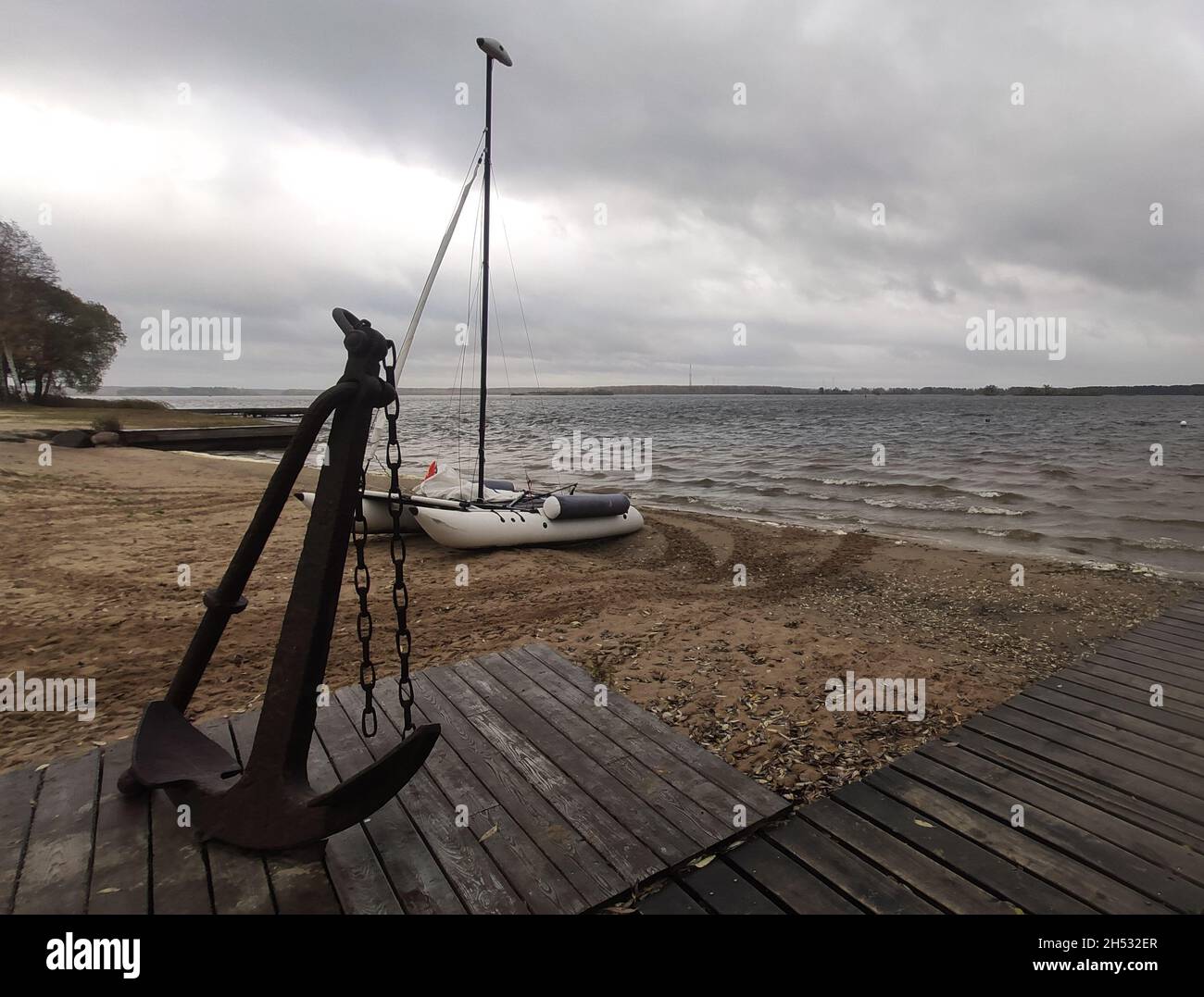 Grande ancienne ancre rouillée sur la jetée en bois sur la rive sablonneuse de la Volga avec le bateau gonflable et la rivière elle-même sur le fond Banque D'Images