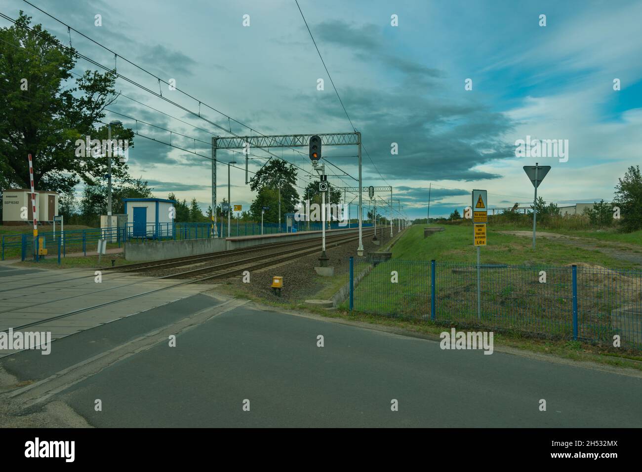 Route asphaltée entrecoupant une voie ferrée à double voie avec traction électrique. Banque D'Images