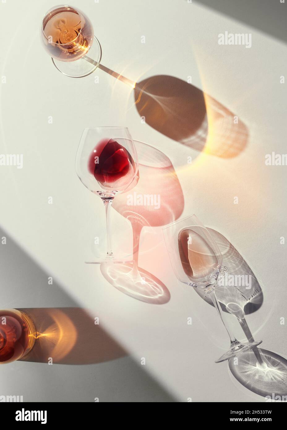 Verres de vin rouge et de rose sur une table blanche.Forte lumière émotionnelle avec ombres dures.Réfractions et colorées. Banque D'Images