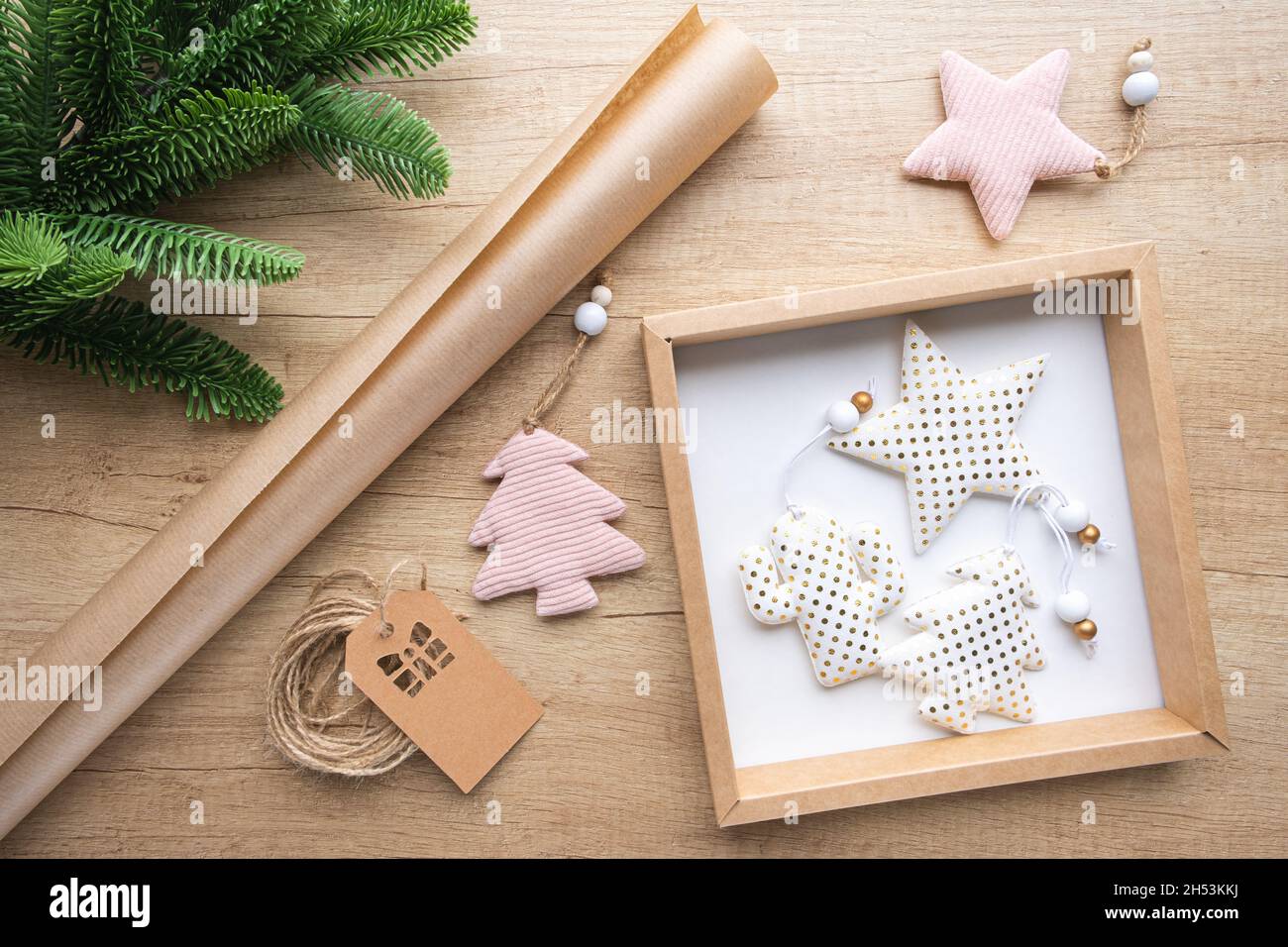 Boîte cadeau avec jouets de Noël en tissu blanc à pois d'or, rouleau de papier kraft, branche de sapin sur fond de bois.Concept d'emballage écologique, zéro Banque D'Images