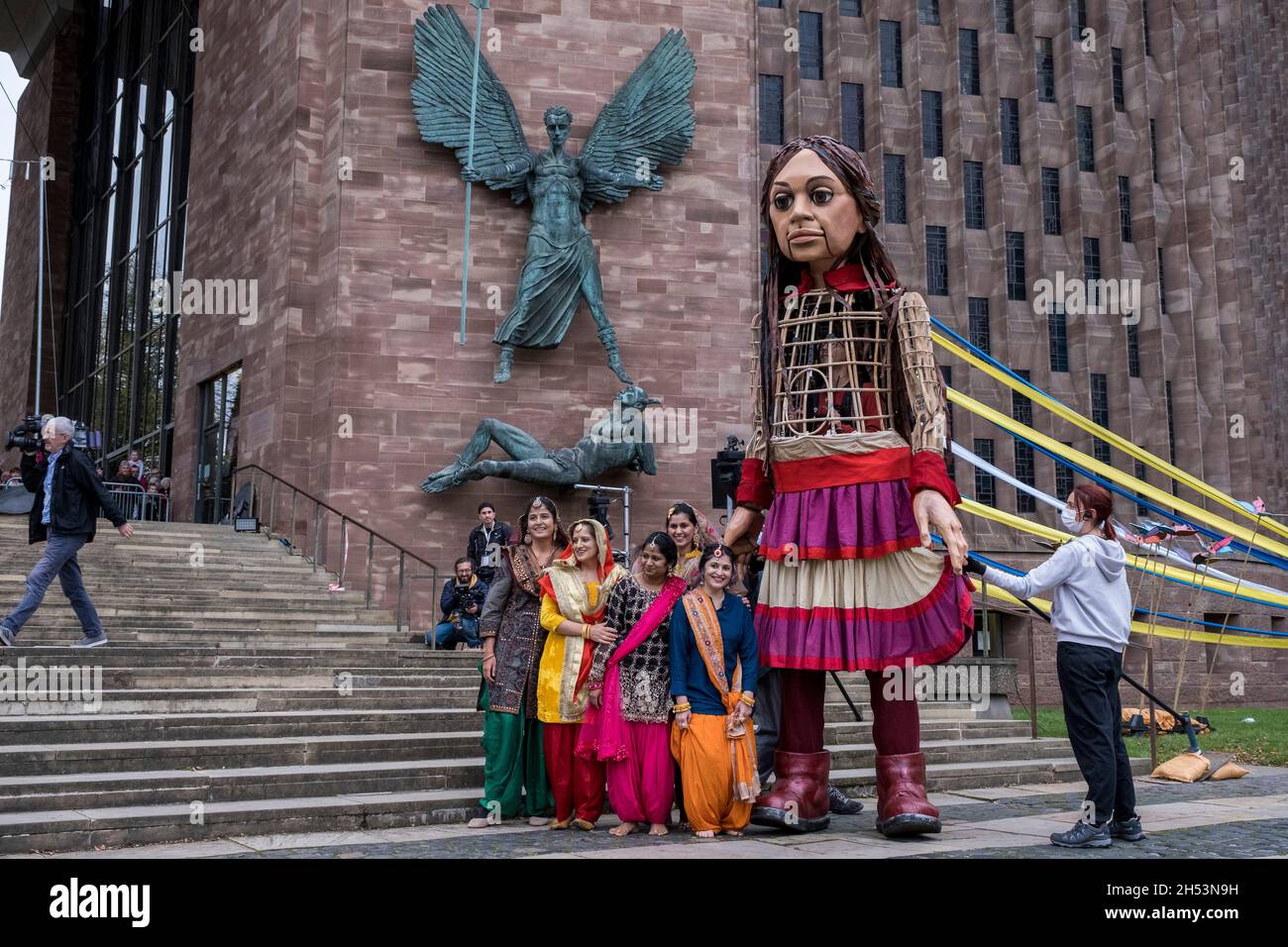 Little Amal enchante les foules de spectateurs lorsqu'elle se promène dans le centre-ville, que l'on voit ici danser avec des danseurs asiatiques dans des saris lumineux devant la cathédrale de Coventry le 27 octobre 2020 à Coventry, au Royaume-Uni.Little Amal est une marionnette de 3.5 mètres de haut et une œuvre d'art vivante d'un jeune enfant réfugié syrien qui a passé les 3 derniers mois à marcher 8000 km de la frontière syrienne à travers la Turquie, la Grèce, l'Italie, la France, la Suisse,L'Allemagne, la Belgique et le Royaume-Uni doivent attirer l'attention sur les besoins urgents des jeunes réfugiés.Coventry, qui a le plus grand programme de réinstallation en Syrie de la région, et aussi un la Banque D'Images