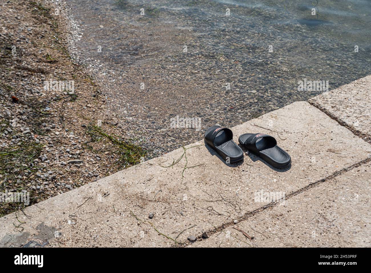 KOPER, SLOVÉNIE - 12 JUILLET 2021 : pantoufles de plage sur un bloc de béton sur une plage de galets au-dessus de la mer Adriatique. Banque D'Images