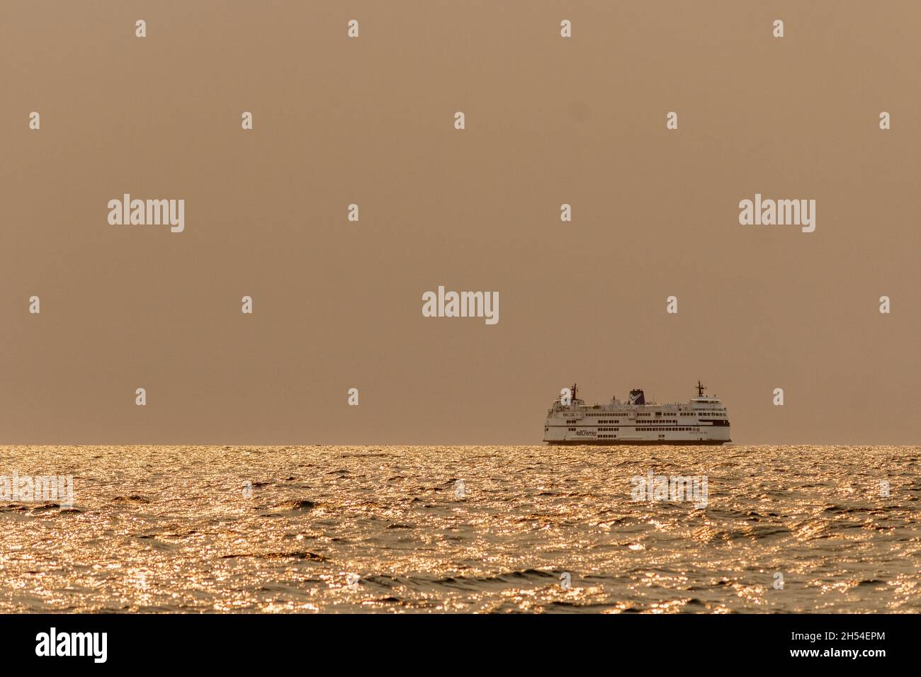 Un traversier pour passagers traverse le détroit de Géorgie un matin d'été, avec une épaisse fumée provenant des feux de forêt qui obscurcissent le soleil et qui fait tourner la mer et le ciel orange. Banque D'Images