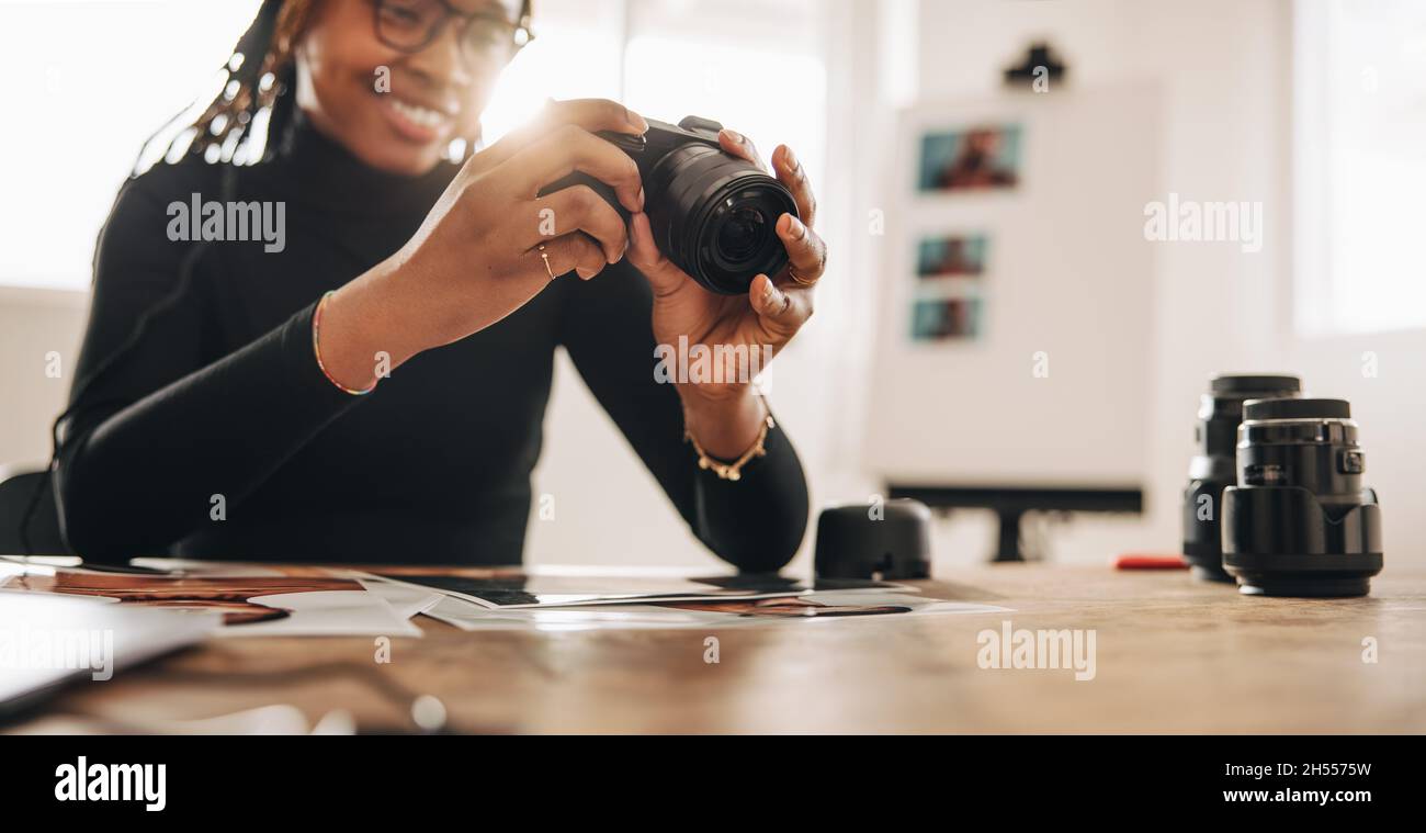 Femme tenant un appareil photo reflex numérique dans son bureau à domicile.Jeune photographe créatif souriant joyeusement tout en travaillant à son bureau.Femme freelance travaillant sur Banque D'Images
