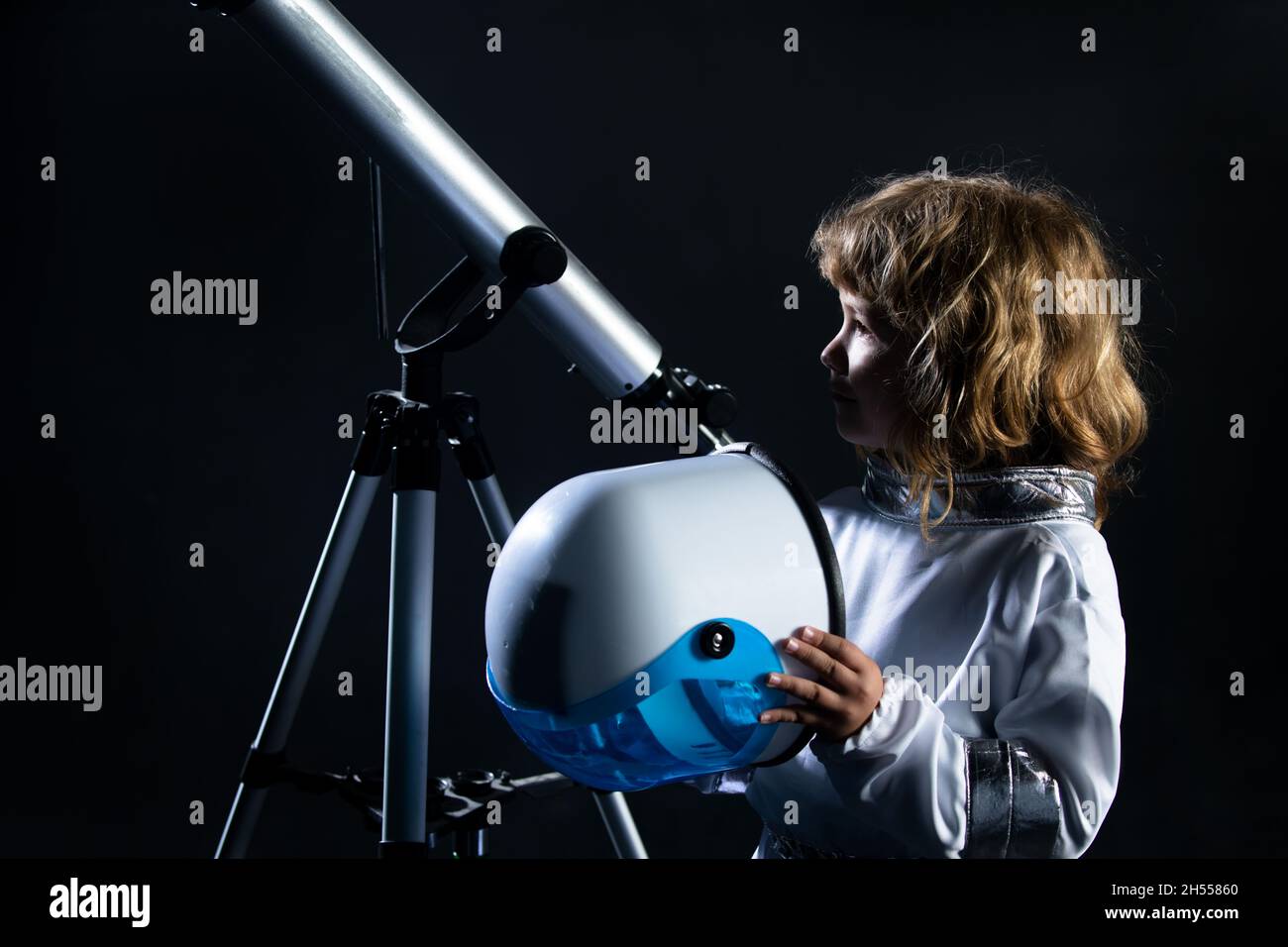 Garçon jouant pour être un astronaute avec un casque d'espace et une combinaison en métal.Portrait d'un gamin drôle avec casque d'astronaute sur fond noir. Banque D'Images