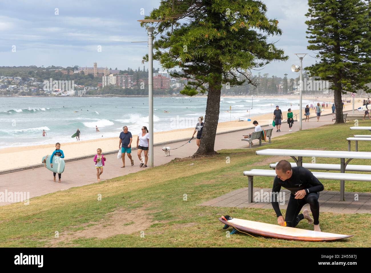 Manly Beach Sydney, surfeur mâle sur sa planche de surf, les gens marchent le long de la côte de l'océan, NSW, Australie Banque D'Images