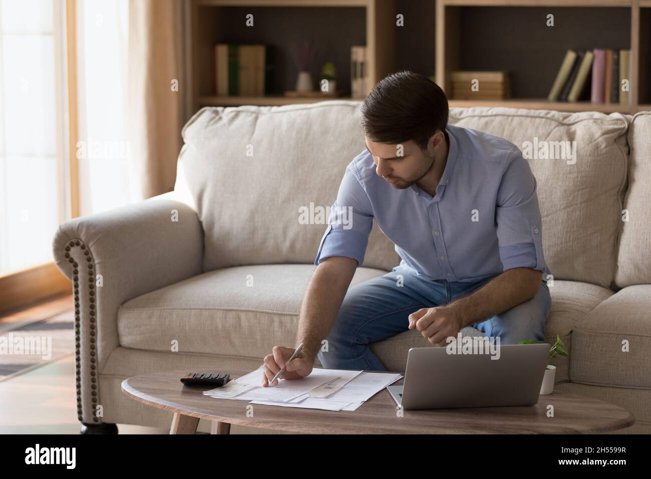 Jeune homme concentré gérant le budget du ménage à la maison. Banque D'Images