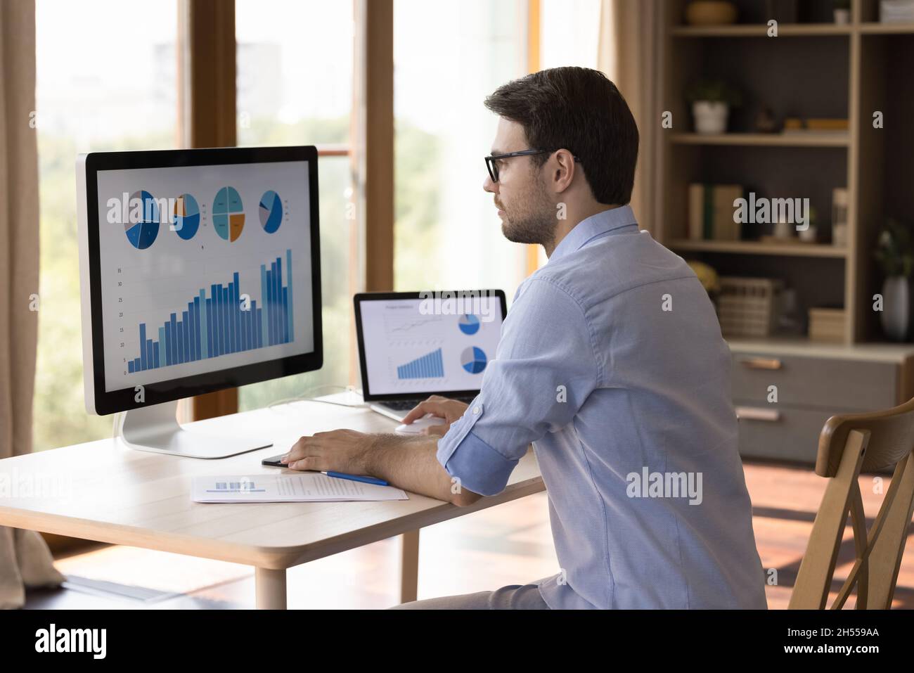 Un jeune homme d'affaires intelligent et ciblé utilisant des gadgets pour analyser les statistiques. Banque D'Images