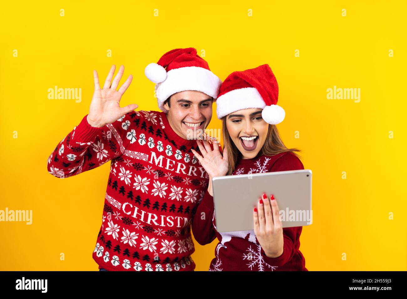 jeune couple latin ayant des appels vidéo de noël à l'aide d'une tablette numérique ou d'un pavé tactile sur un fond jaune Banque D'Images jeune couple latin ayant des appels vidéo de noël à l'aide d'une tablette numérique ou d'un pavé tactile sur un fond jaune Banque D'Images