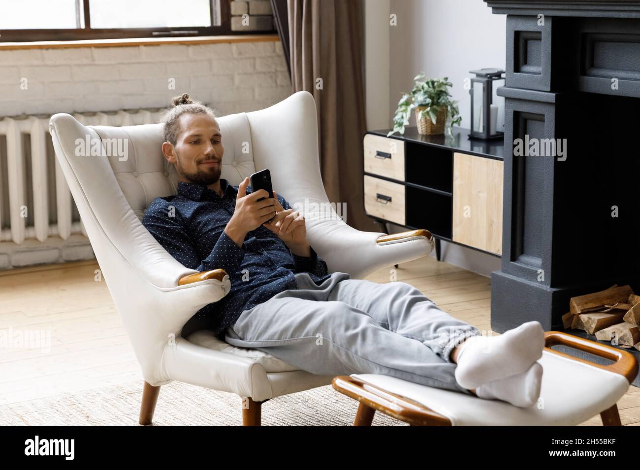 Joyeux décontracté jeune homme hippster utilisant un téléphone portable, assis dans un fauteuil. Banque D'Images