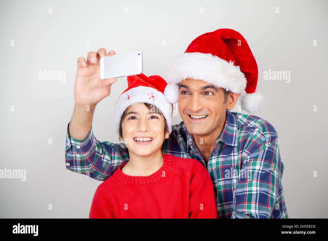 Un père et un fils souriants portant un chapeau de Noël prenant des selfies sur fond blanc Banque D'Images