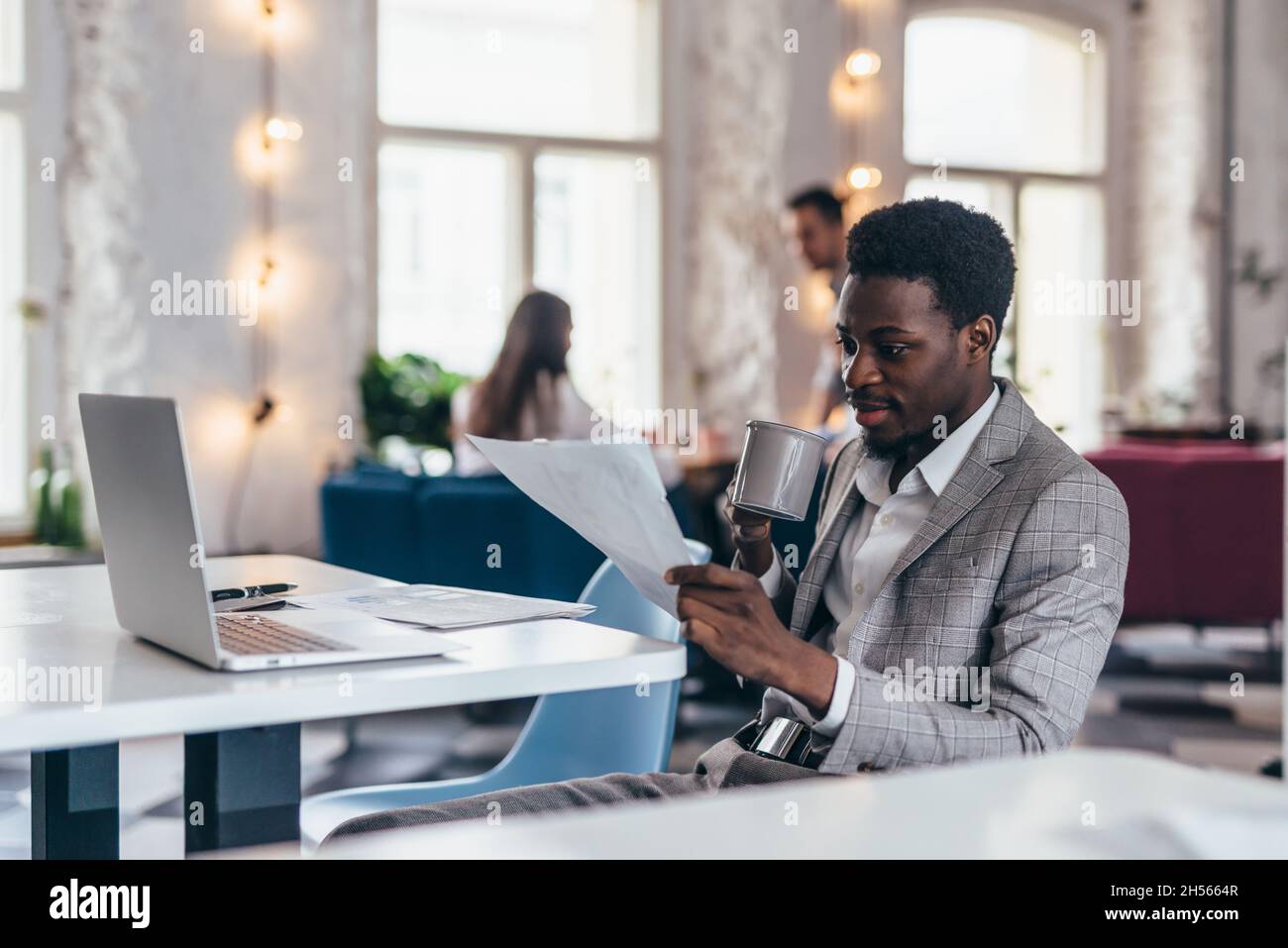 Homme d'affaires dans un café lisant le document de contrat.Cadre d'affaires africain assis dans un café en activité. Banque D'Images
