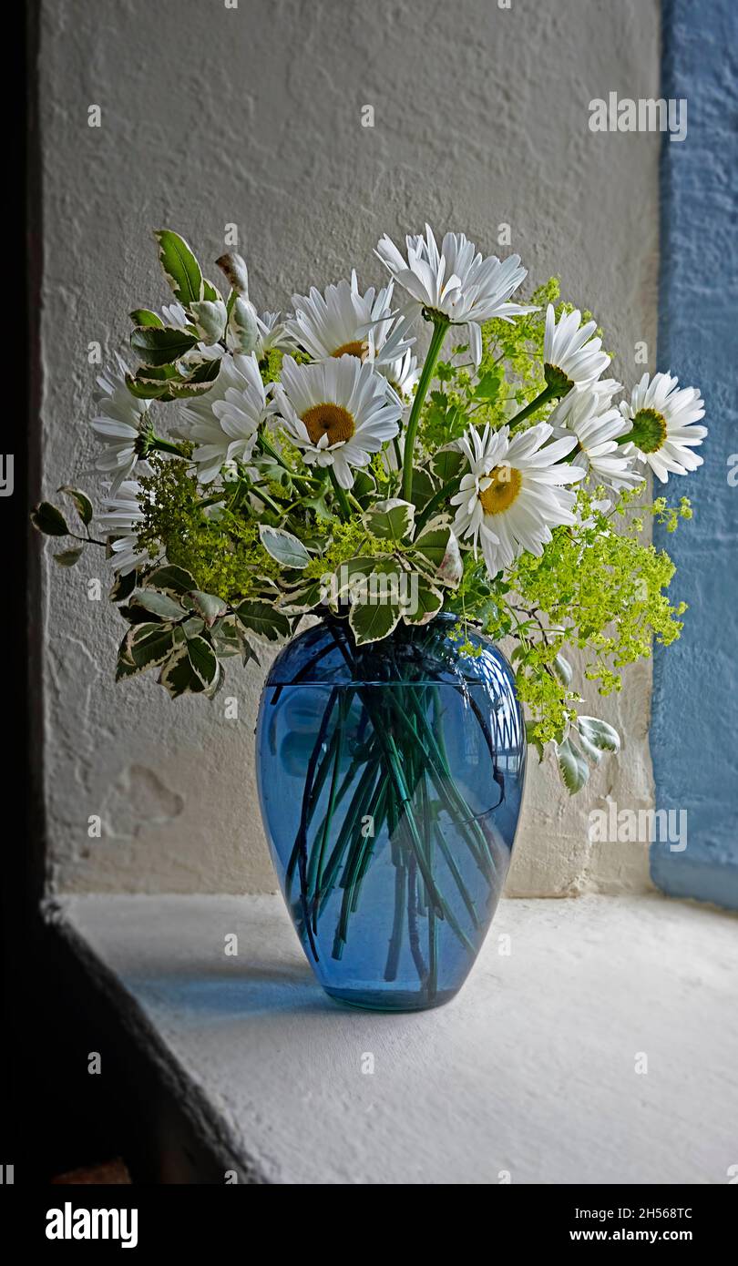 Pâquerettes et autres fleurs dans un vase en verre bleu dans une fenêtre d'église dans l'Irlande de Cork Ouest Banque D'Images
