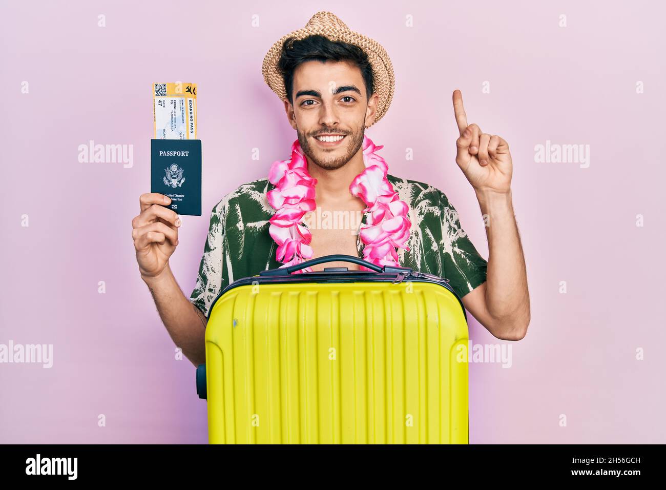 Jeune homme hispanique portant un style estival et un lei hawaïen tenant un passeport et une carte d'embarquement souriant avec une idée ou un doigt de pointage de question avec happ Banque D'Images