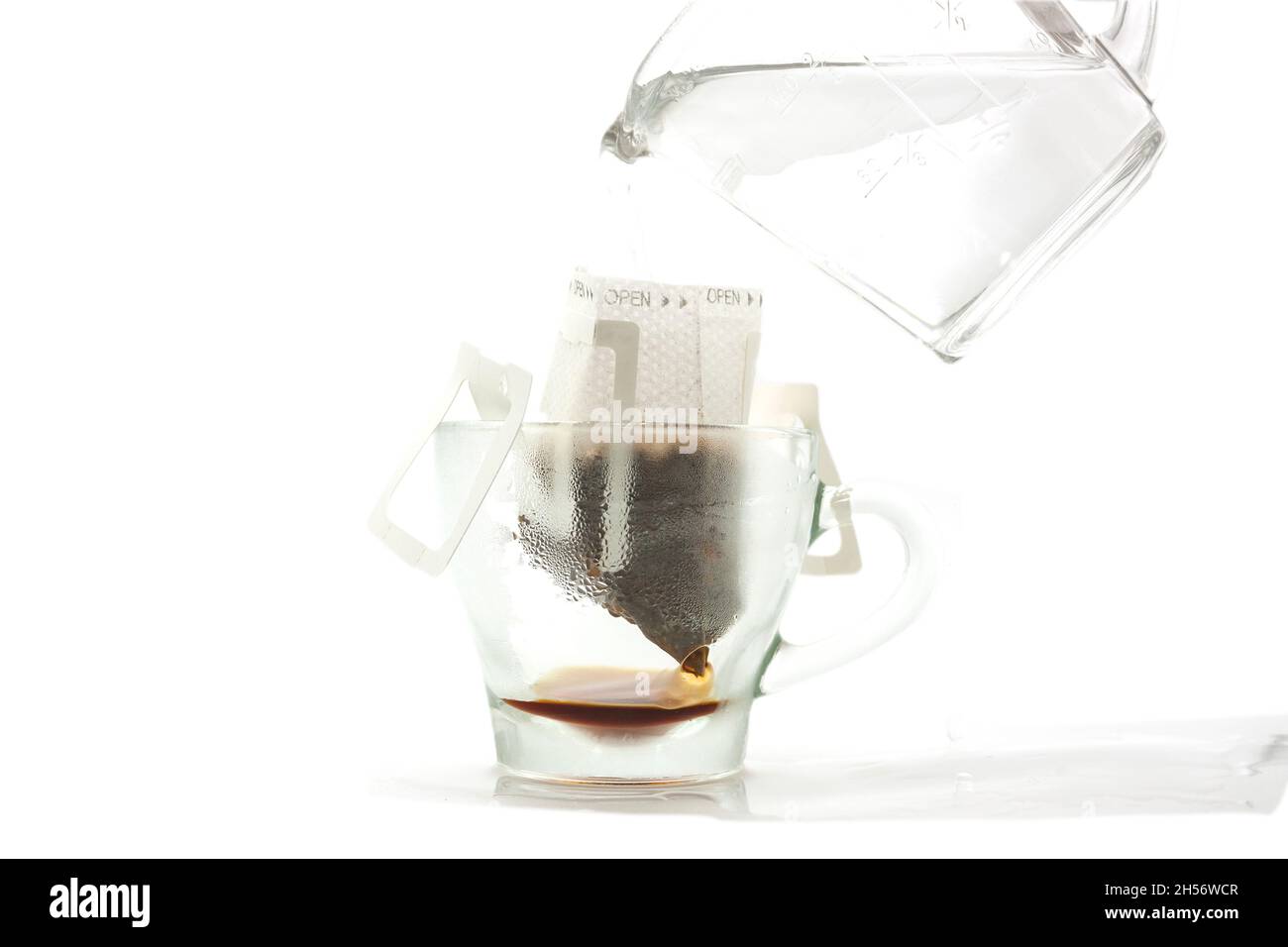 eau chaude en verre de condensation servie par une tasse dans un sac filtre en papier pour faire du café américain isolé fond blanc gouttes d'eau tombent sur le comptoir Banque D'Images