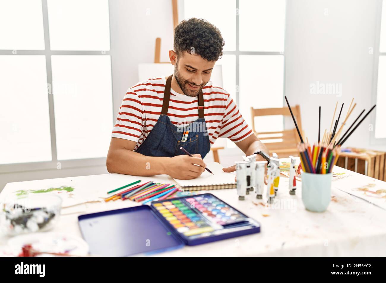 Jeune artiste arabe homme souriant dessin heureux au studio d'art. Banque D'Images