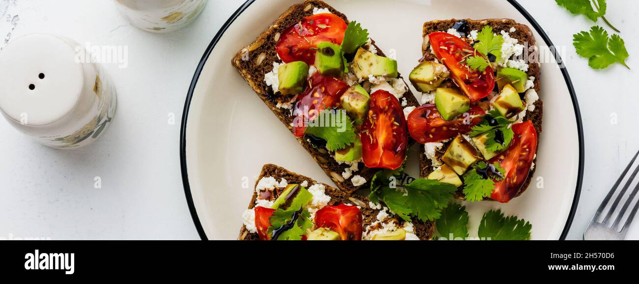 Des avocats, des tomates cerises et des sandwiches au fromage feta avec sauce balsamique et coriandre sur un vieux plateau d'olives.Vue de dessus. Banque D'Images