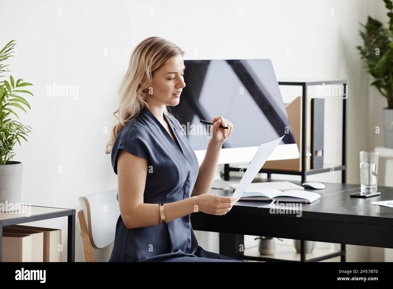 Portrait de femme d'affaires blonde élégante avec vue latérale, lisant des documents tout en travaillant au bureau, dans un espace de travail Banque D'Images