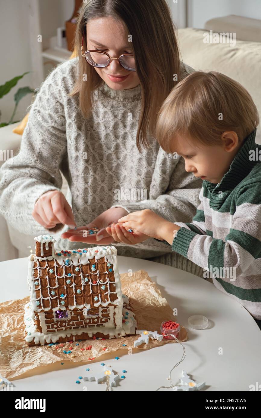 Petit garçon avec mère décorant la maison de pain d'épice de noël ensemble, activités familiales et traditions à Noël et le nouvel an Banque D'Images