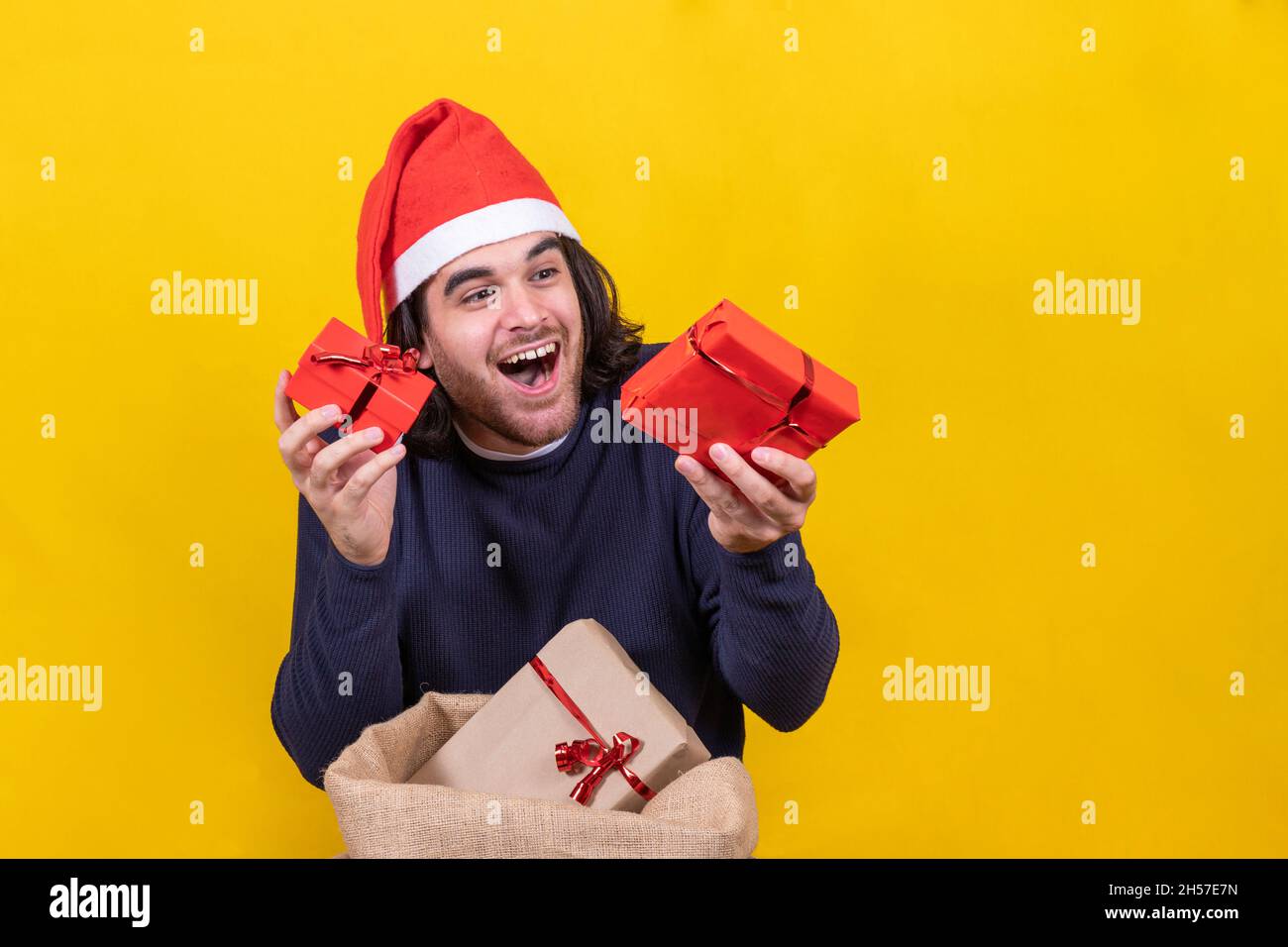 Un jeune homme dans un chapeau de Père Noël montre des cadeaux de Noël heureux.Fond jaune pour un portrait de studio.Joyeux Noël concept. Banque D'Images