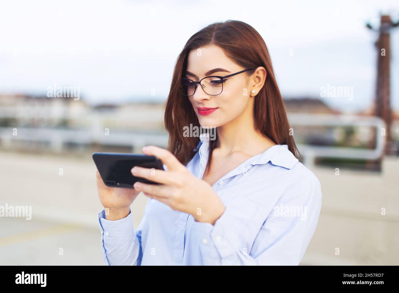 Jeune femme d'affaires caucasienne astucieuse à tête rouge messagerie sur smartphone à l'extérieur Banque D'Images