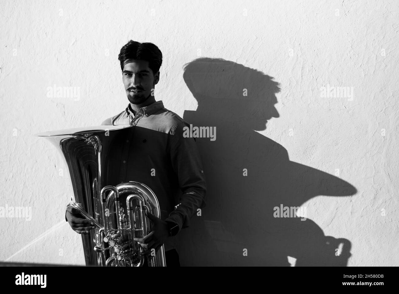 Un musicien masculin avec un tuba et son ombre sur un mur blanc.Photo en noir et blanc. Banque D'Images