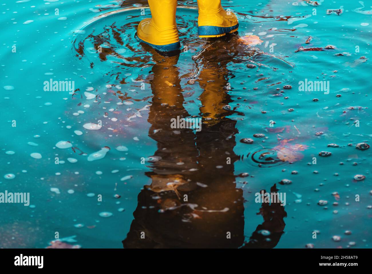 Enfant avec bottes de pluie en caoutchouc marchant sur un trottoir humide en automne après-midi, attention sélective Banque D'Images