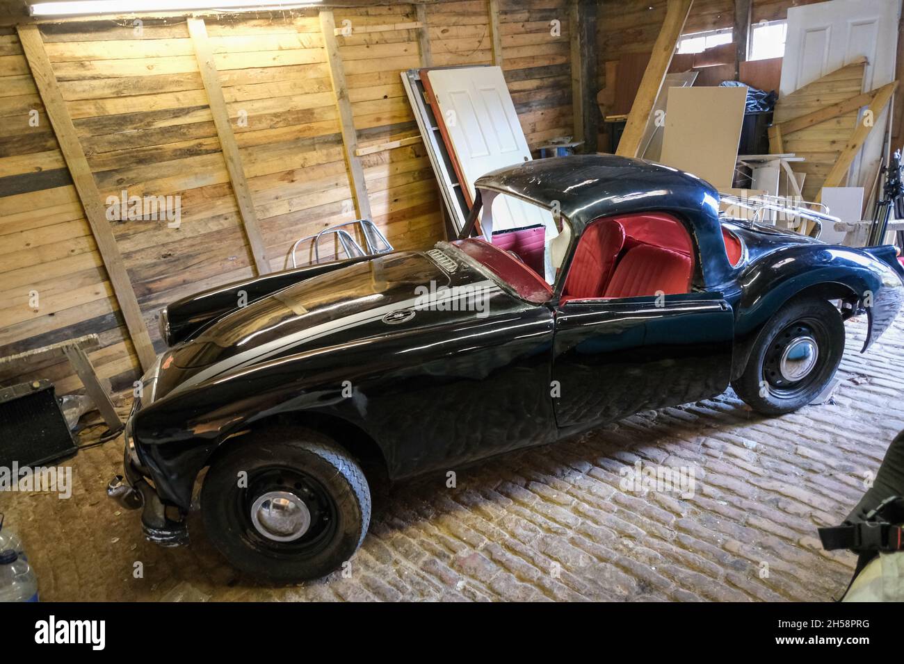Un coupé noir 1950s MGA projets de restauration garés dans un garage désordonné Banque D'Images