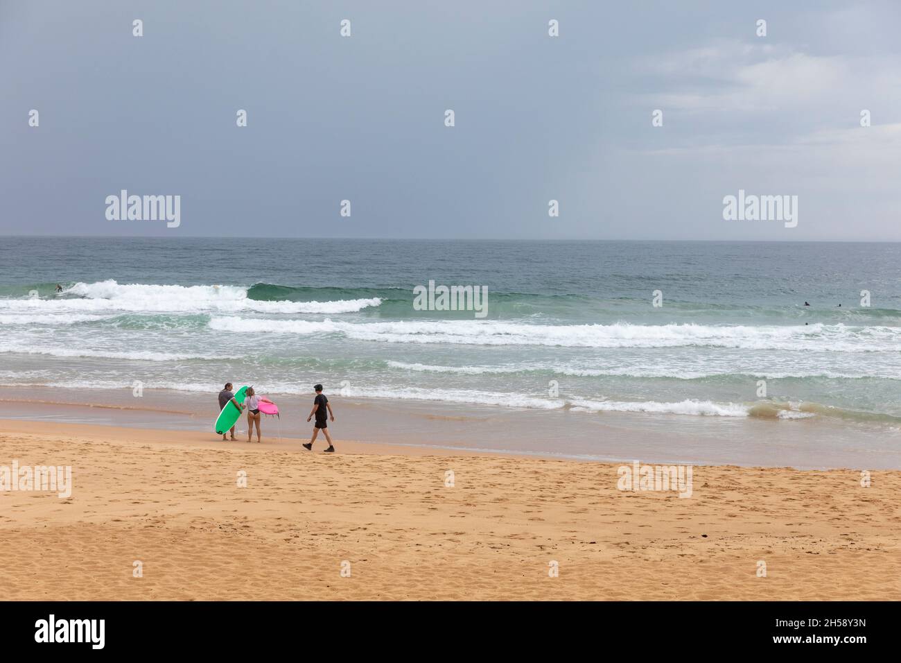 Deux surfeurs se tenaient sur la plage de Manly pendant que l'homme se promenait dans les sentiers d'exercice noirs, journée découverte de Sydney, Australie Banque D'Images