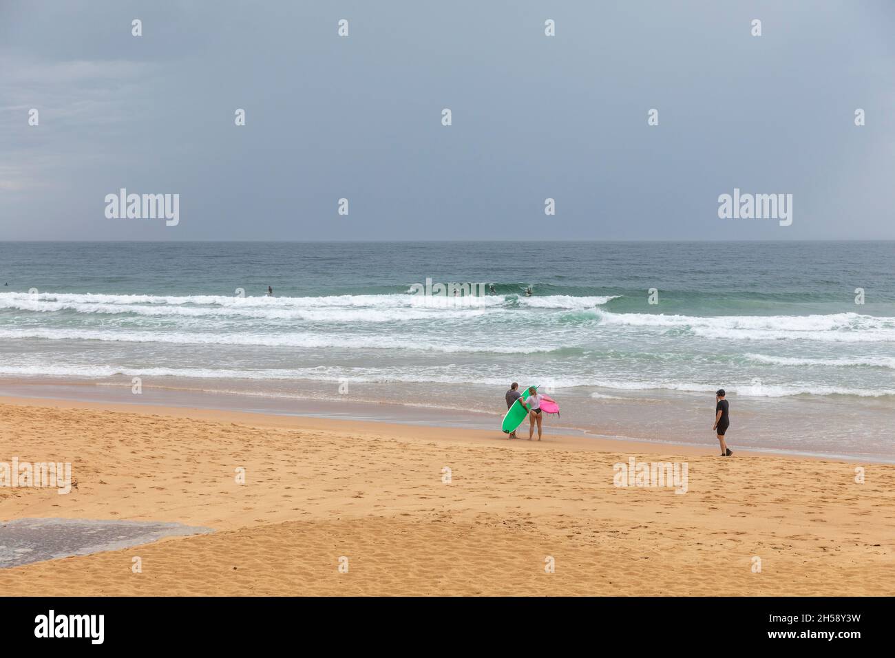 Deux surfeurs sur Manly Beach, météo printanière sauvage et ciel gris, Sydney, Australie Banque D'Images