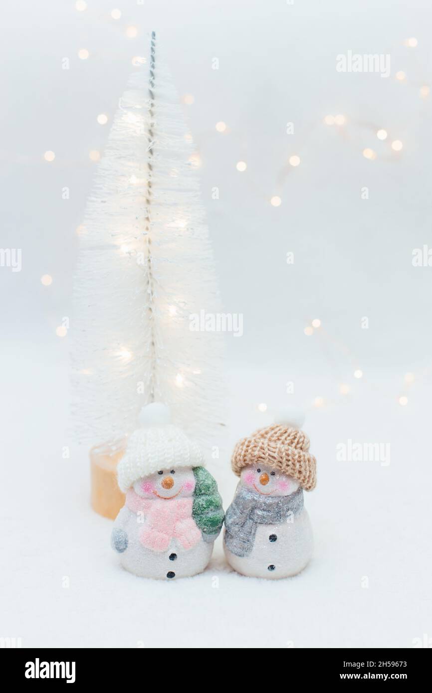 Figurines décoratives sur le thème de Noël.Deux statuettes d'un bonhomme de neige dans un chapeau tricoté sur fond blanc.Décoration festive, lumières bokeh chaleureuses Banque D'Images