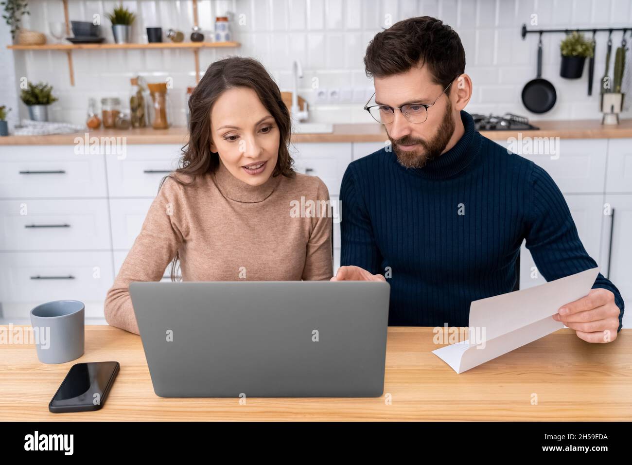 Un couple familial qui fait les factures de services publics assis à la cuisine à la maison à l'aide d'un ordinateur portable Banque D'Images