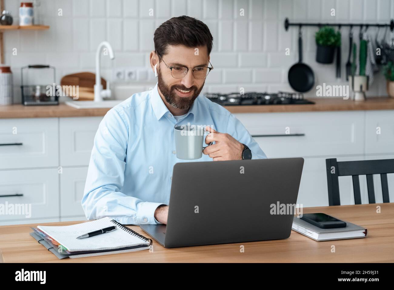 L'homme d'affaires boit du café en travaillant sur un ordinateur portable tenant une vidéoconférence en ligne Banque D'Images