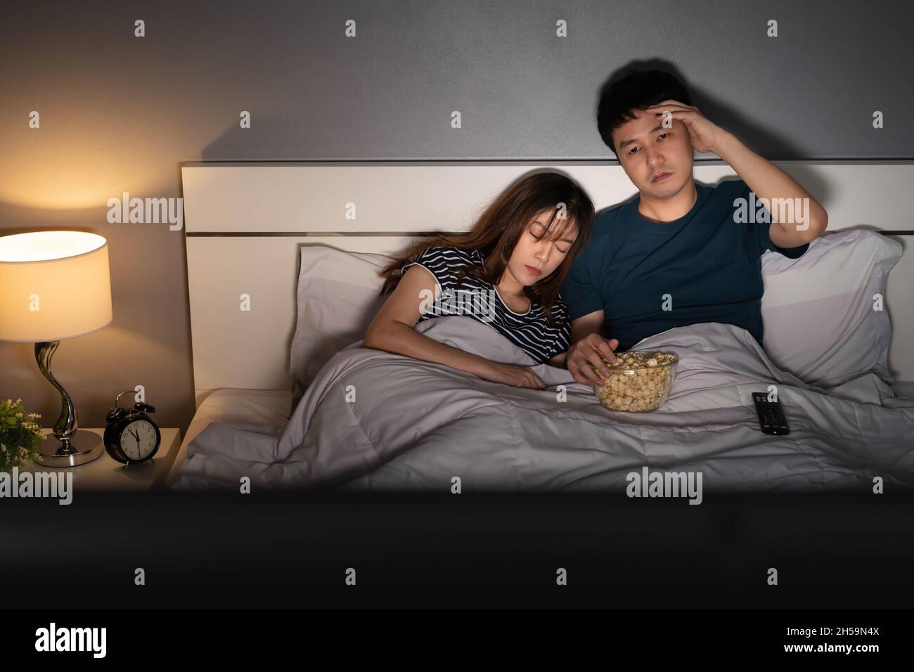 jeune homme regardant la télévision dans son lit avec sa femme. expression somnolente et fatiguée souffrant d'insomnie Banque D'Images