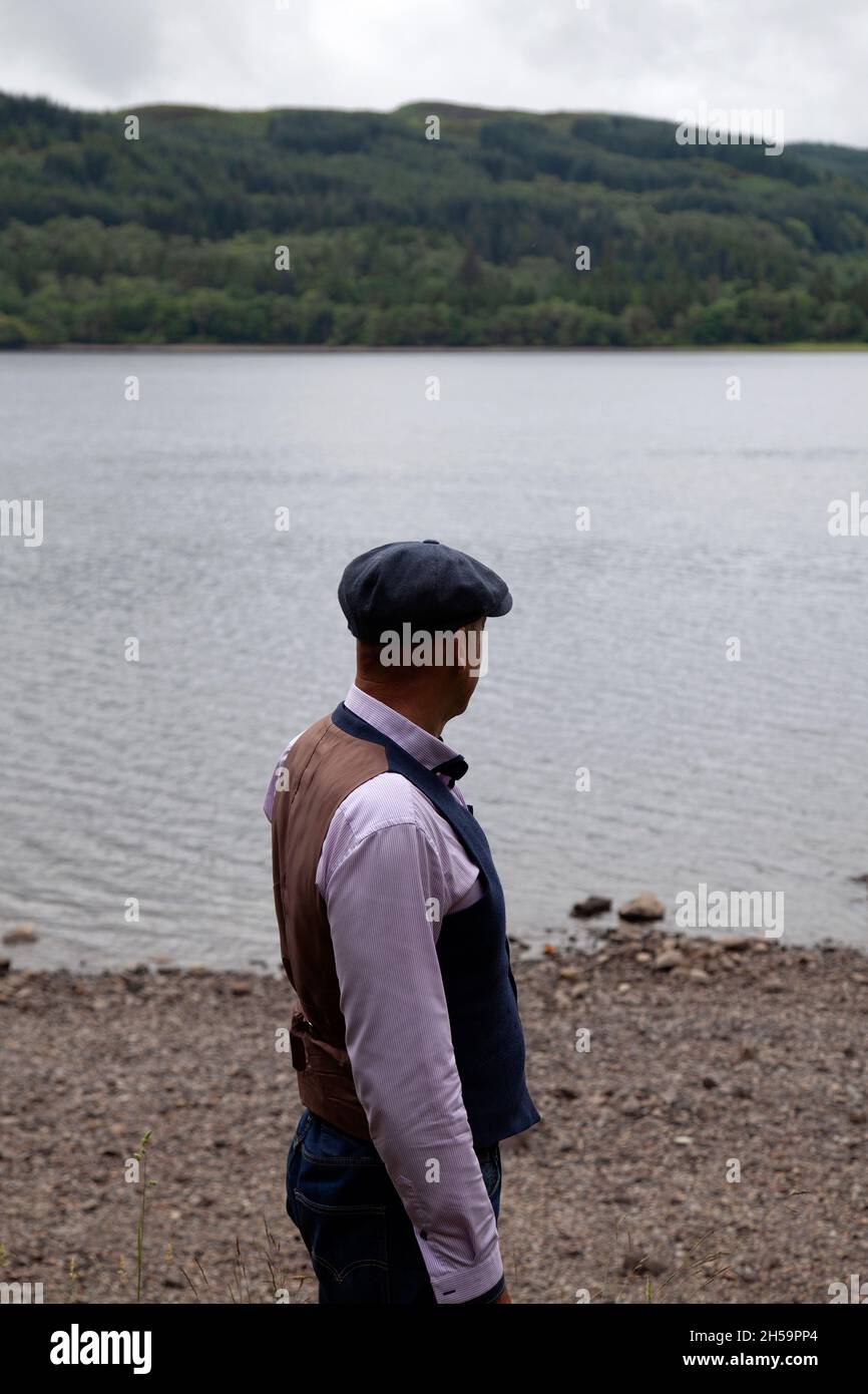 Homme en gilet de costume et jeans debout près du lac Banque D'Images