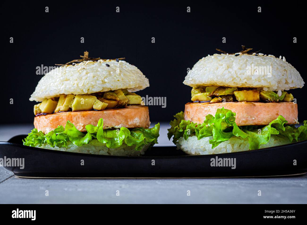 Hamburger de riz avec escalopes de saumon, sauce à l'avocat et au soja, fond noir. Banque D'Images