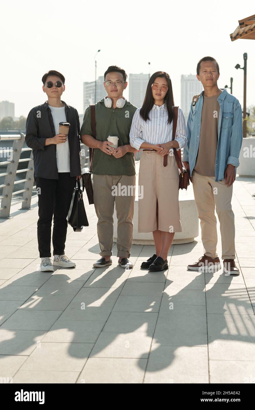 Rangée de quatre jeunes collègues chinois en vêtements décontractés debout devant la caméra en milieu urbain Banque D'Images
