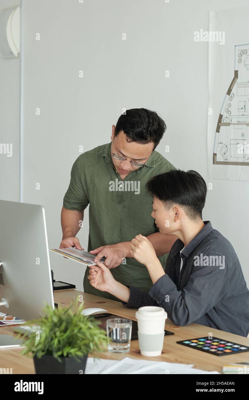 Deux jeunes designers d'origine asiatique discutent d'échantillons de couleurs pour un nouveau projet lors d'une réunion de travail au bureau Banque D'Images