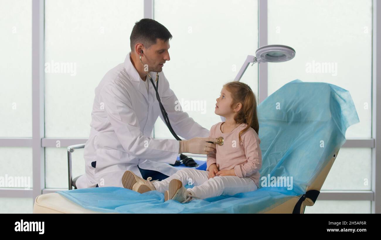 Un enfant visite le cabinet du médecin.Le docteur écoute les poumons de l'enfant avec un stéthoscope, parle avec Caringly la petite fille. Banque D'Images