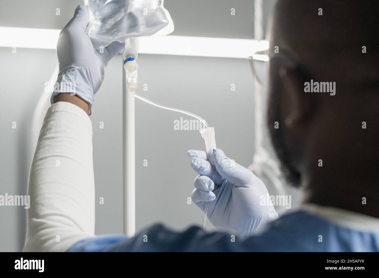 Vue arrière de l'anesthésiste africain travaillant avec perfusion goutte-à-goutte pendant l'opération dans la salle d'hôpital Banque D'Images