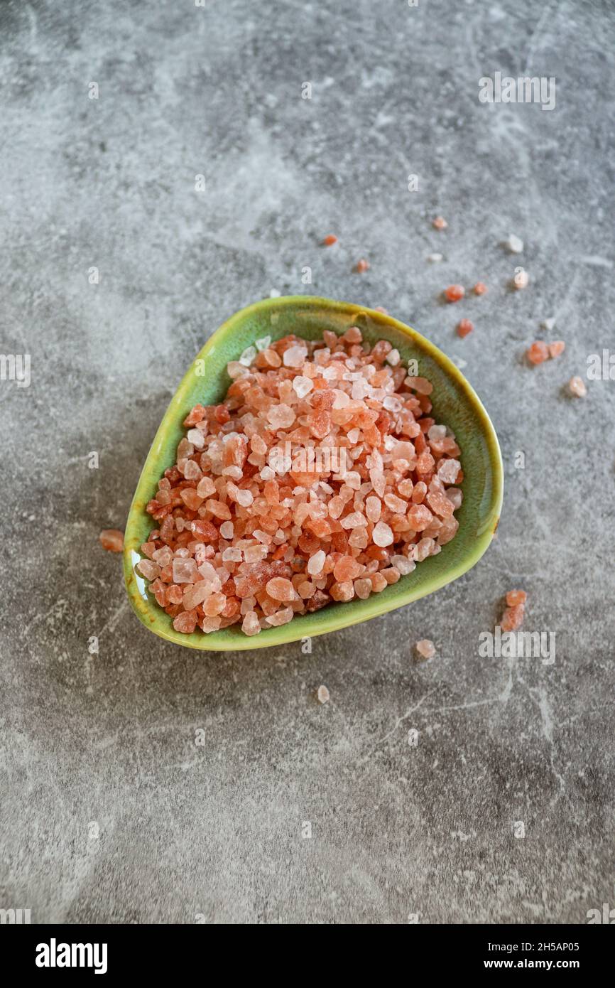 Roche himalayenne rose gros sel dans une petite assiette verte sur fond gris Banque D'Images